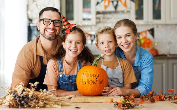 Счастливая мать семьи, отец и двое детей улыбаются перед камерой с тыквой во время празднования, готовясь дома Хэллоуин украшения - Фото, изображение