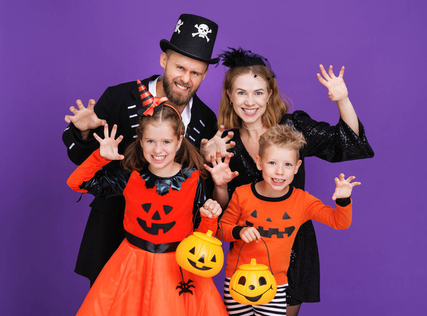 Веселая семья мать отец и дети в карнавальных костюмах делает страшный жест праздновать Хэллоуин на цветном фиолетовом фоне - Фото, изображение
