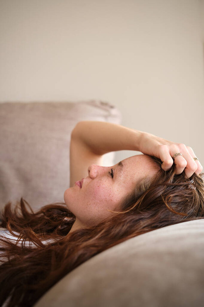 Κάθετη κοντινή φωτογραφία μιας νεαρής γυναίκας ξαπλωμένης στον καναπέ με πονοκέφαλο - Φωτογραφία, εικόνα
