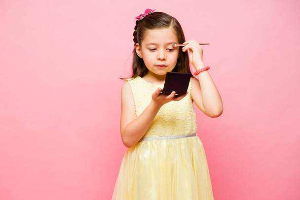 Kavkazský krásný holčička hrát uvedení na make-up a baví se s kosmetickými produkty v přední růžové pozadí - Fotografie, Obrázek
