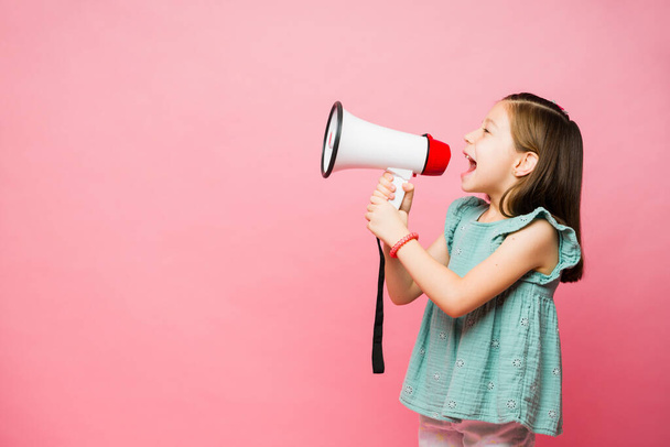 Caucásico niño de 7 años de edad dando un fuerte mensaje de los niños y gritando con un megáfono en frente de un fondo de copia rosa - Foto, Imagen
