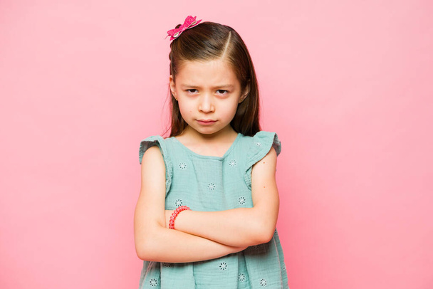 Angry caucasian little child looking upset and annoyed while feeling bored because of kids problems in a pink background - Photo, Image