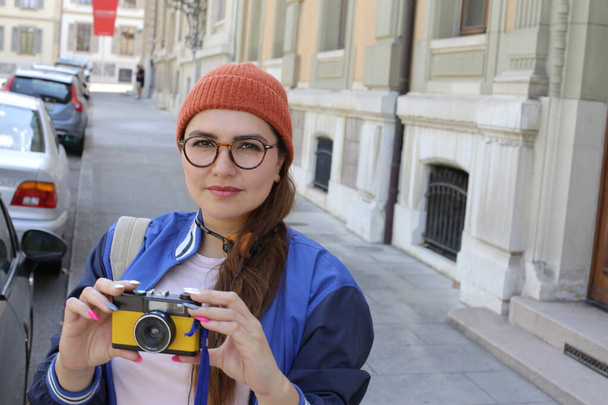 retrato de mujer hermosa joven en ropa hipster con estilo con auriculares vintage y cámara de cine en la calle de la ciudad - Foto, Imagen