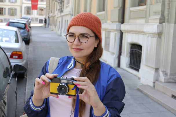 portrait of young beautiful woman in stylish hipster clothes with vintage headphones and film camera on city street - Photo, Image