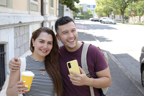 portrait de jeune couple heureux avec tasse en papier de café et smartphone sur la rue de la ville ensemble - Photo, image