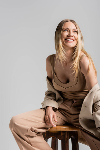 close up of happy smiling blonde woman in beige formal suit sitting on chair, fashion concept - Фото, изображение