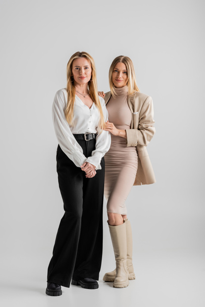 aantrekkelijke stijlvolle zussen in formele outfit poseren op grijze achtergrond, hechting, mode concept - Foto, afbeelding