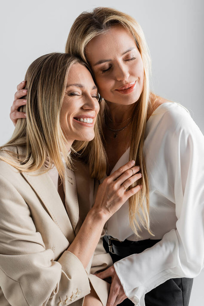 twee stijlvolle aantrekkelijke zussen in formele dragen knuffelen elkaar en glimlachen, mode concept - Foto, afbeelding