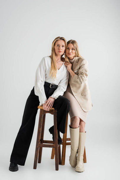 two fashionable stylish sisters in formal outfits sitting on chairs, fashion and style concept - Photo, Image