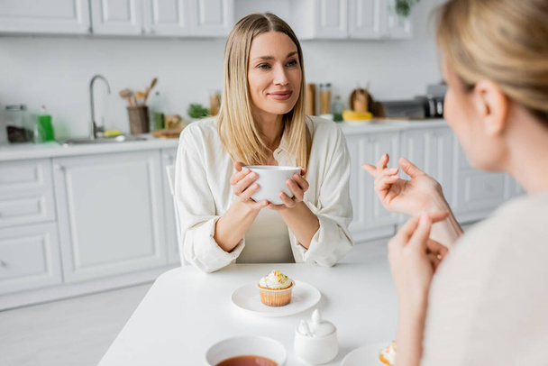 ostříhaný pohled na krásné sestry mluví a těší čaj s kuchyňským pozadím, lepení - Fotografie, Obrázek