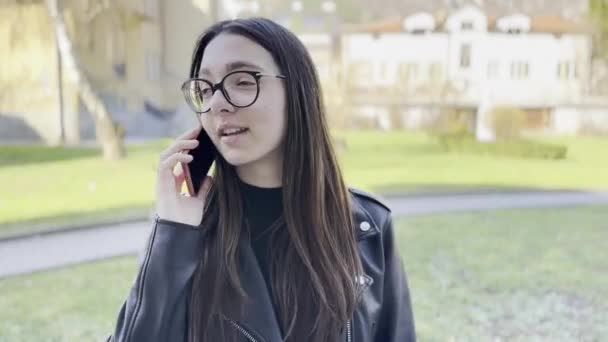 Adolescente habla en el teléfono inteligente mientras está de pie en el parque.  - Metraje, vídeo