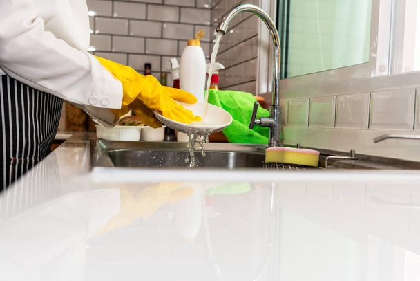 Casalinga con guanti di gomma gialla che lava i piatti. alle persone e al concetto di lavori domestici. - Foto, immagini