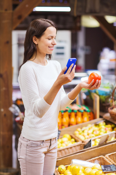 happy woman with smartphone and tomato in market - 写真・画像
