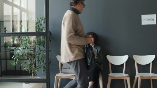 Plan complet moyen d'un homme caucasien mature et d'une jeune femme noire venant au hall assis à côté d'une femme caucasienne à lunettes, des femmes tenant des smartphones, toutes en attente d'une interview - Séquence, vidéo