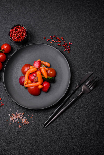 Lahodný čerstvý šťavnatý salát s ředkvičkami, rajčaty, mrkví, okurkou, kořením a bylinkami na tmavém betonovém pozadí - Fotografie, Obrázek