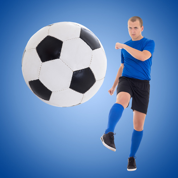νεαρός ποδοσφαιριστής που κλωτσάει την μπάλα πάνω από το μπλε - Φωτογραφία, εικόνα