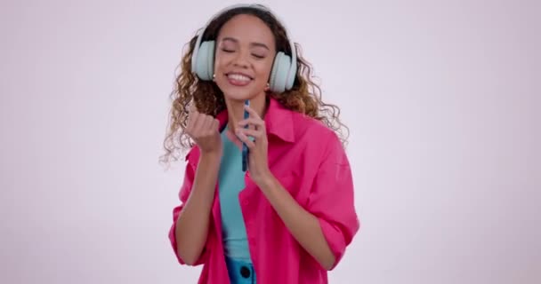 Face of woman, singing and dance with headphones in studio to celebrate freedom, party and excited on white background. Portrait of happy model dancing for karaoke, cellphone and listening to music. - Footage, Video
