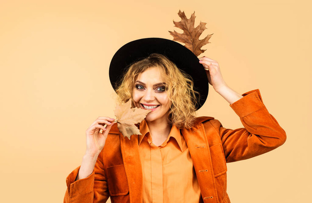Bela menina sorridente em roupas de outono na moda com folhas de outono. Moda mulher de outono em chapéu preto com folhas de bordo amarelas. Roupas de outono elegantes para mulheres. Folha a cair. Vendas de outono. Desconto - Foto, Imagem
