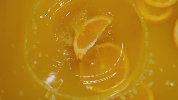 Κοντινό πλάνο της πτώσης φέτες λάιμ, πορτοκάλια και λεμόνια στο νερό σε πορτοκαλί φόντο, κάνοντας ένα κοκτέιλ εσπεριδοειδών, πίνοντας κρύα λεμονάδα, ρίψη ανθρακούχου νερού με φέτες φρούτων. - Πλάνα, βίντεο