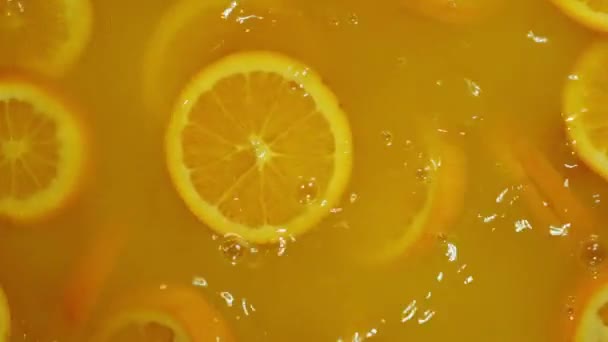 Zbliżenie spadających limonek w plasterkach, pomarańczy i cytryn do wody na pomarańczowym tle, zrobienie koktajlu z owoców cytrusowych, picie zimnej lemoniady, strzelanie do wody gazowanej z plasterkami owoców. - Materiał filmowy, wideo