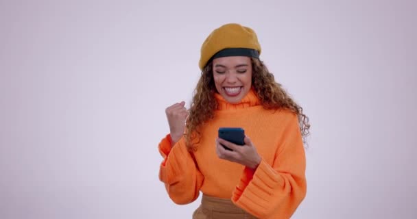 Happy woman, phone and winning in celebration, good news or promotion against a studio background. Excited female person with fist pump on mobile smartphone in success, achievement or discount sale. - Footage, Video