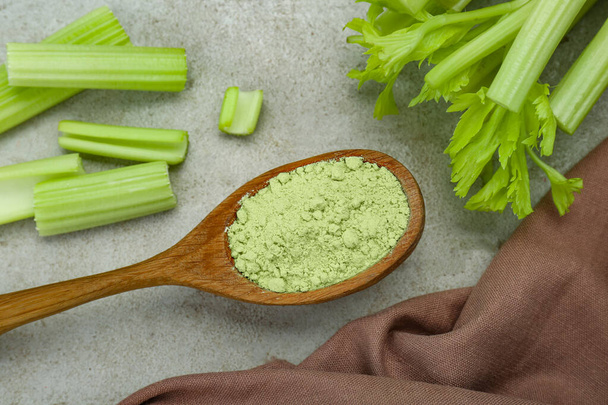 Natural celery powder in wooden spoon and fresh stalks on grey table, flat lay - Foto, afbeelding