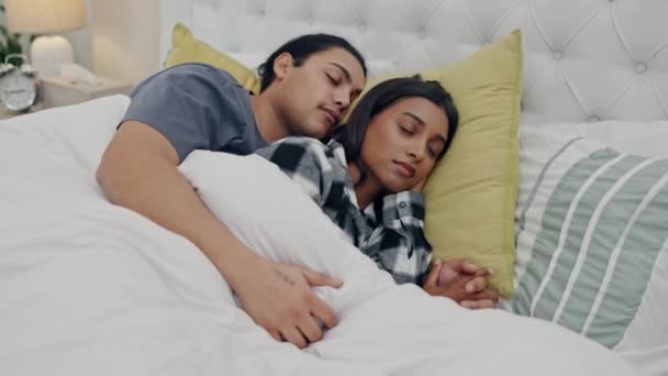 Fatigue, rest and couple sleeping in bed and holding hands for tired morning, romance and love. Relax, cuddle and young man and woman taking nap and dreaming together in bedroom of a modern home - Footage, Video