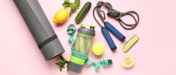 Sportovní láhev okurkové limonády s podložkou na jógu, skákacím lanem a měřicí páskou na růžovém pozadí - Fotografie, Obrázek