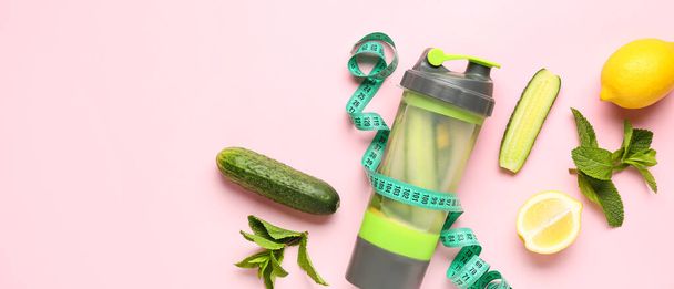 Sportfles komkommer limonade met meetlint op roze achtergrond met ruimte voor tekst - Foto, afbeelding