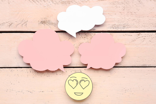 Cara de papel con ojos de corazón y burbujas de habla en blanco sobre fondo de madera beige - Foto, Imagen