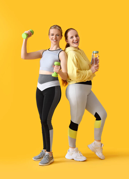 Porträt sportlicher junger Frauen mit Hanteln und Wasser auf gelbem Hintergrund - Foto, Bild