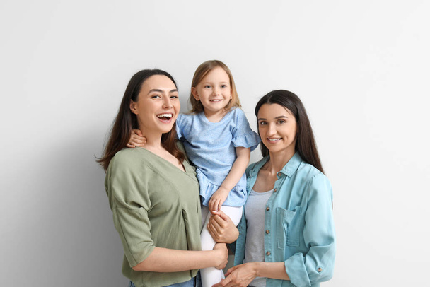 Young lesbian couple with adopted little girl on light background - Photo, Image