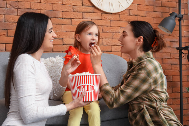 Giovane coppia lesbica con adottato bambina mangiare popcorn a casa - Foto, immagini