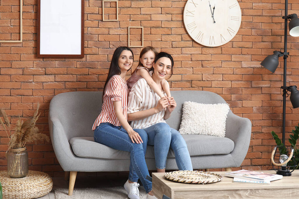 Mladé lesbičky pár s adoptovanou holčičkou sedí na pohovce doma - Fotografie, Obrázek