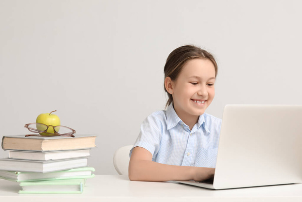 Aranyos kislány laptoppal csinál házi feladatot az asztalnál a fényfal közelében - Fotó, kép