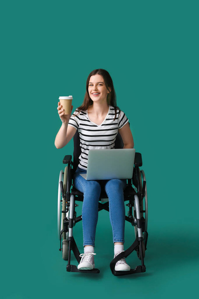 Junge Frau mit Kaffeetasse mit Laptop im Rollstuhl auf grünem Hintergrund - Foto, Bild