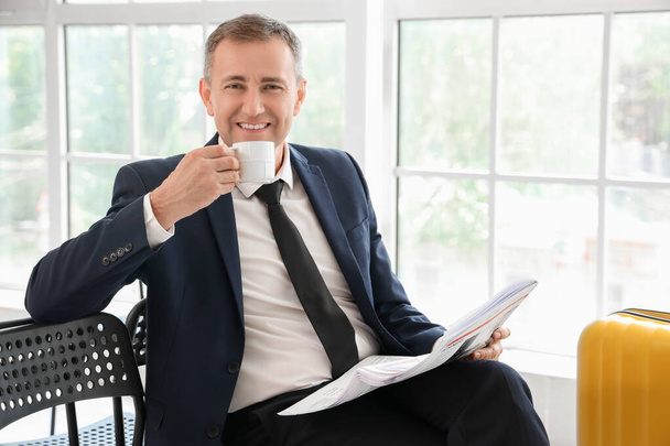 Reifer Geschäftsmann mit Tasse Kaffee beim Zeitungslesen in der Flughafenhalle - Foto, Bild