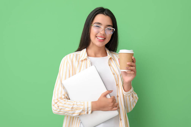 Szczęśliwy młody programistka kobieta z laptopem i filiżanką kawy na zielonym tle - Zdjęcie, obraz