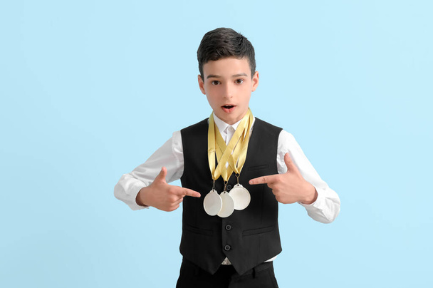 Sorprendido niño de escuela con medallas de oro sobre fondo azul claro - Foto, imagen
