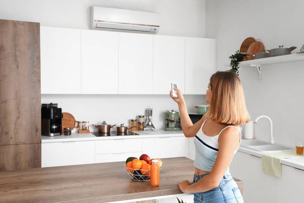 Young woman switching on air conditioner in kitchen - Photo, Image