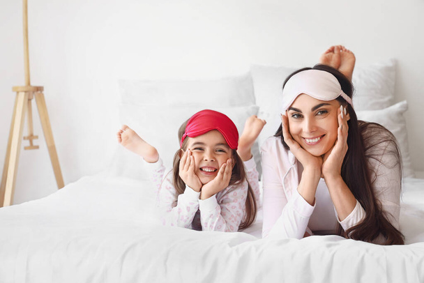 Happy mother and her little daughter with sleeping masks in bedroom - Photo, Image