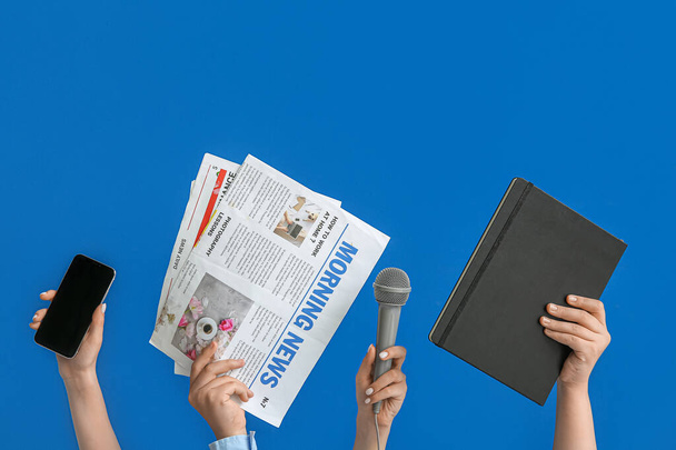 Frauenhände mit Handy, Zeitungen, Mikrofon und Notizbuch auf blauem Hintergrund - Foto, Bild