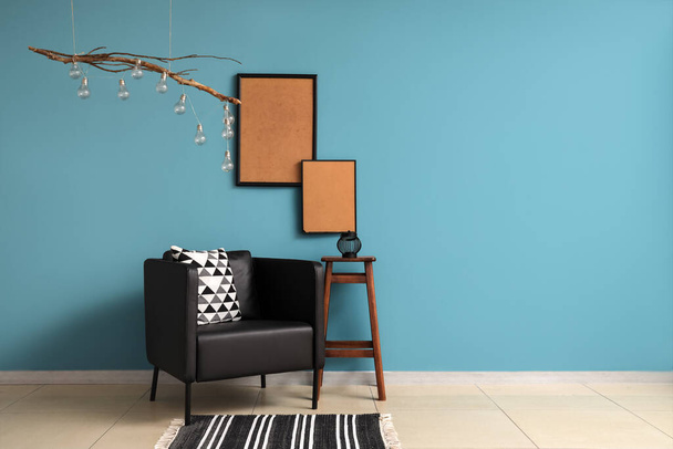 Stilvoller schwarzer Sessel und leere Holzrahmen in der Nähe der blauen Wand - Foto, Bild