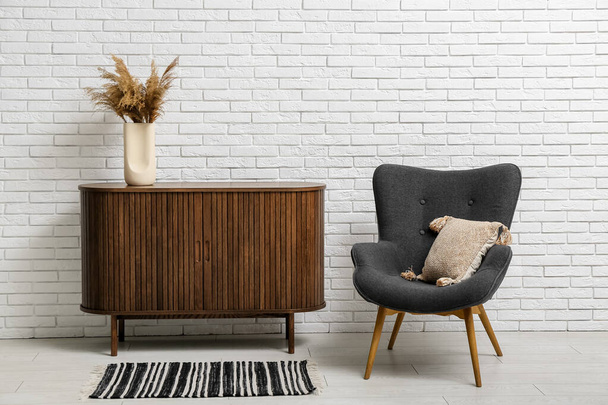 Stylish armchair and wooden cabinet near light brick wall - Photo, Image
