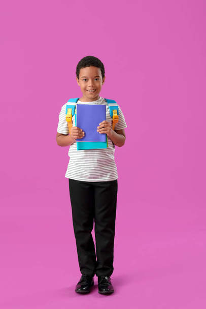 Kis afro-amerikai iskolás fiú stílusos egyenruhában jegyzetfüzetekkel, lila háttérrel - Fotó, kép