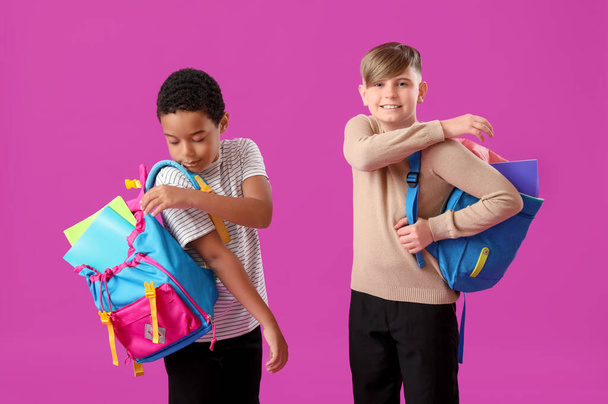 Маленькі однокласники в стильній формі з блокнотами та рюкзаками на фіолетовому фоні - Фото, зображення
