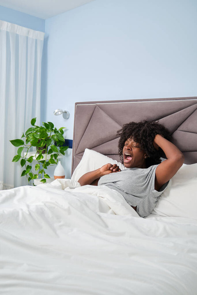 Boldog afrikai mosolygós nő ásít és nyújtózkodik az ágyon reggel. Felébredni egy nyugodt álomból.. - Fotó, kép