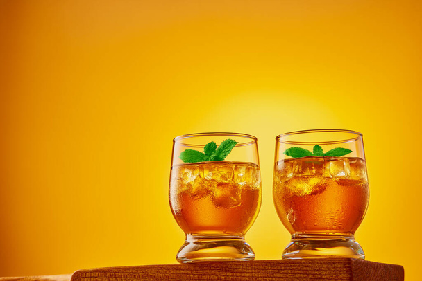 Два стакана освежающего чая со льдом и мятными листьями на оранжевом фоне. Студийный снимок под низким углом с пространством для копирования. - Фото, изображение