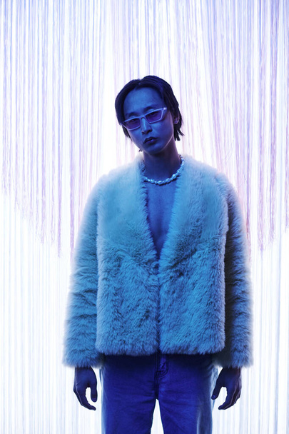 Vertical portrait of extravagant Asian man wearing fur coat at nightclub or party in blue light - Photo, Image
