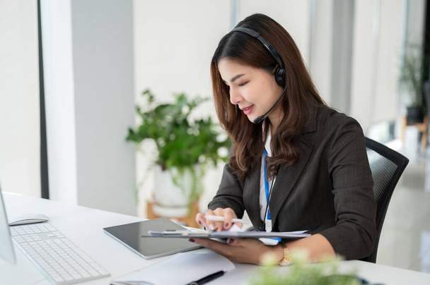 Krásná asijská operátorka call centra nebo agentka zákaznické podpory se sluchátky pracuje u svého stolu v kanceláři. - Fotografie, Obrázek